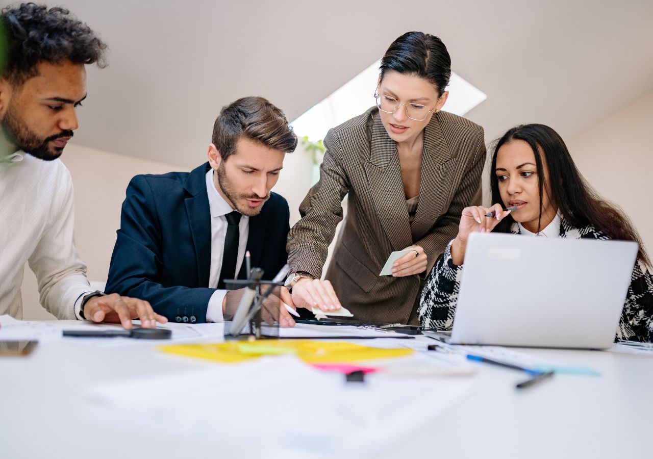 Photo of four people huddling around a computer work desk to illustrate 4 Mistakes New Bosses Make.