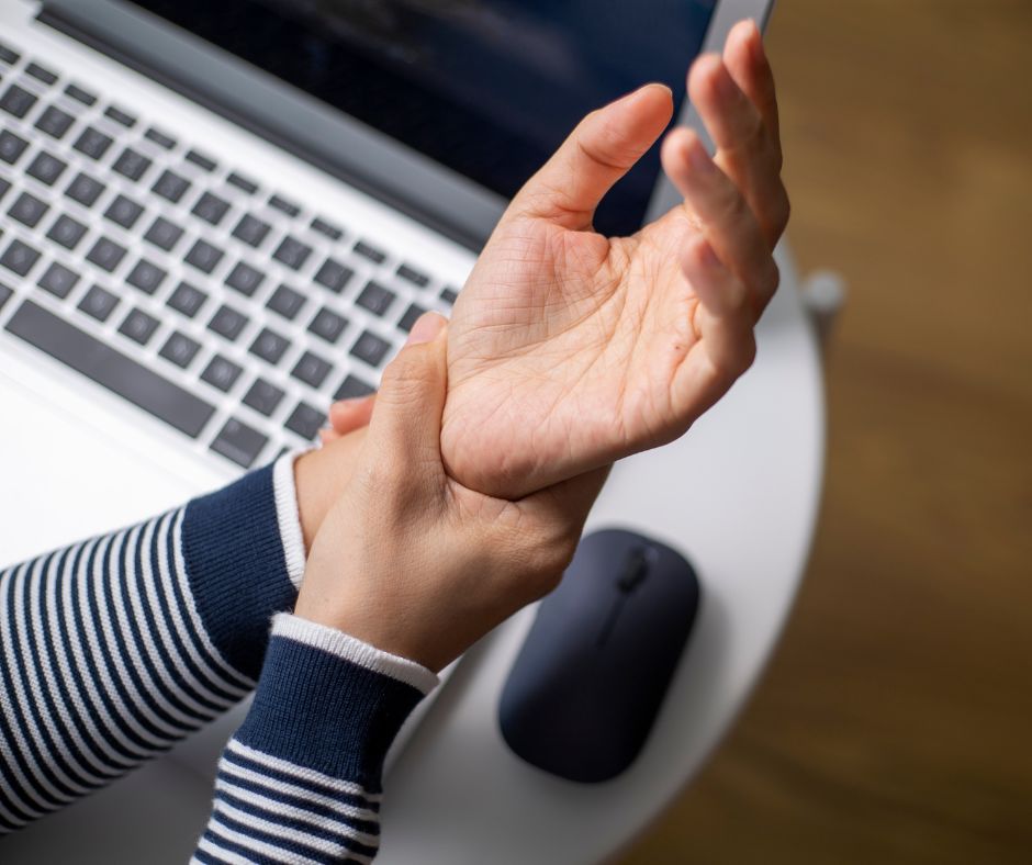 Photo of woman holding her wrist above a computer to illustrate why you should avoid assigning repetitive tasks.