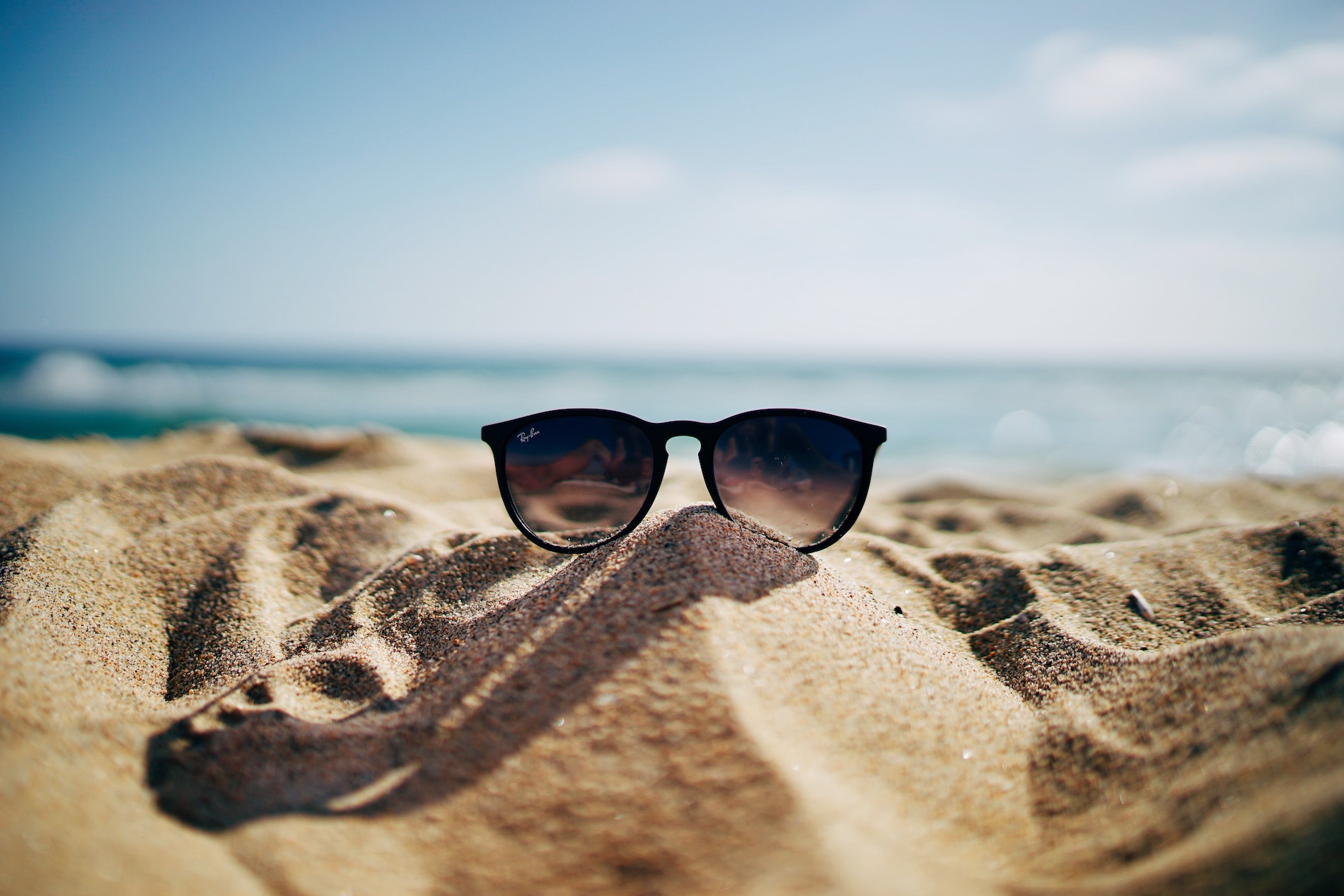 Photo of sunglasses at the beach to illustrated How to Stay Engaged During the Summer.