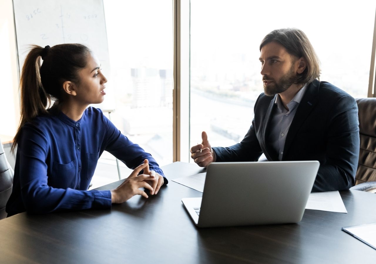 Photo of woman speaking to man in office to illustrate "Should you tell your boss youre job hunting"