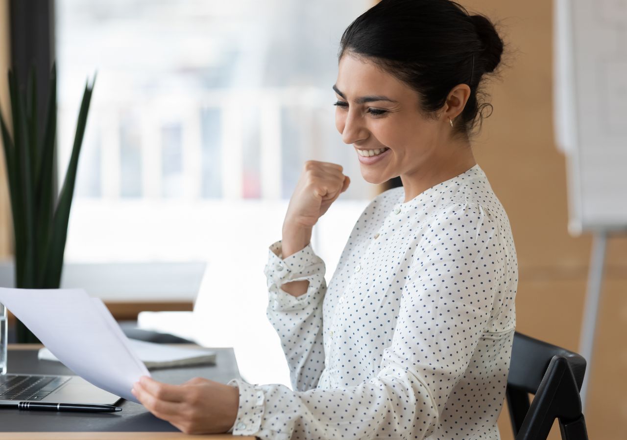 8 qualities you need in an employee Photo of happy woman reading paper to illustrate 8 qualities you need in an employee