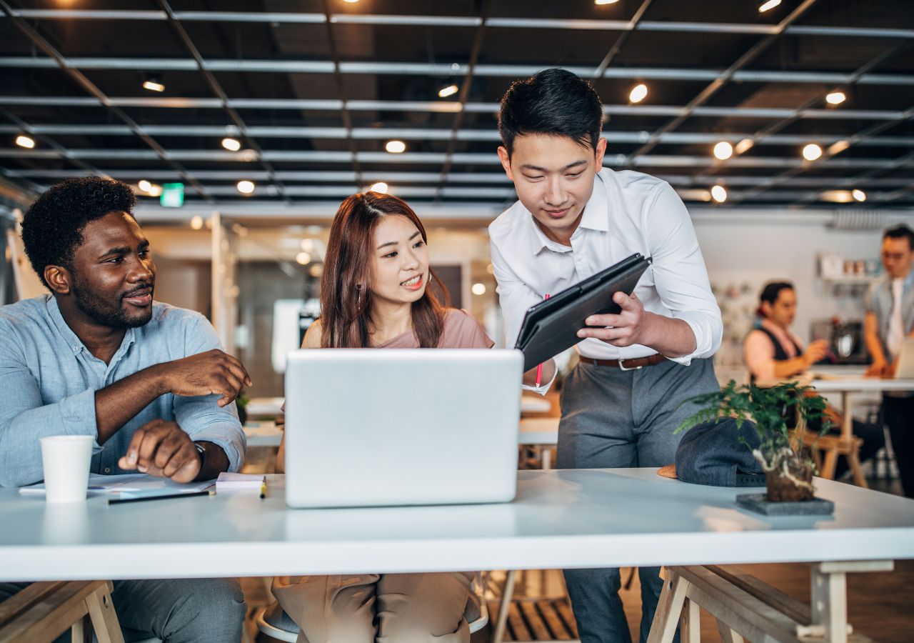 Photo of three workers gather around a laptop and tablet to illustrate How to Identify High-Potential Employees