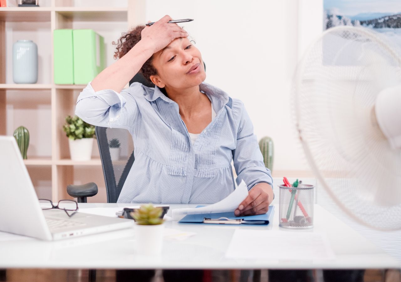 Photo of woman working at a desk with a fan in front of her.