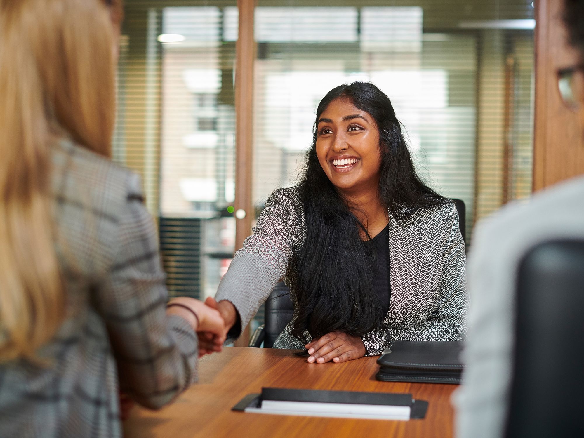 Photo of happy employee looking at another woman shaking hands to identify how to identify a great employee.