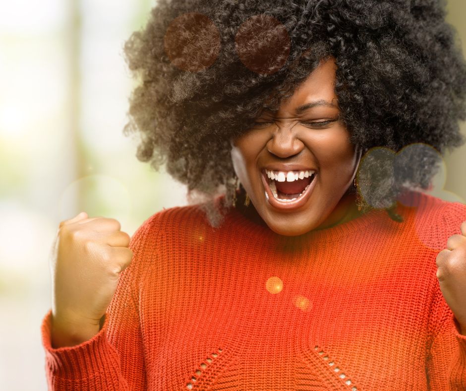 Photo of black woman with orange sweater screaming with excitement to illustrate how to reenter the job market successfully.