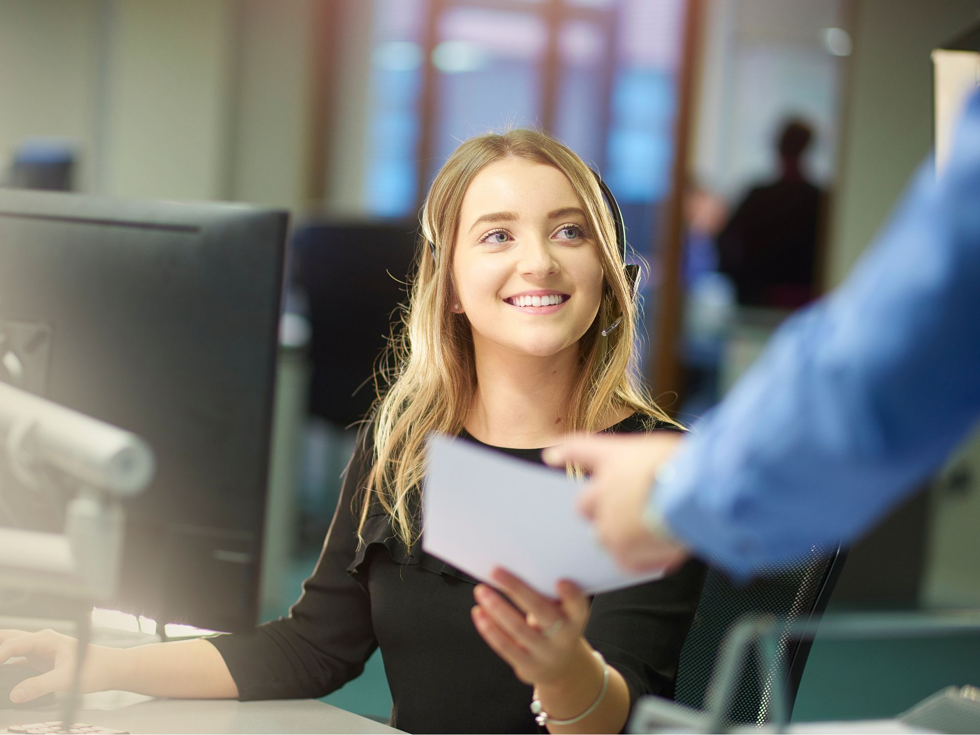 Photo of smiling young woman at computer grabbing a paper to illustrate switching careers.