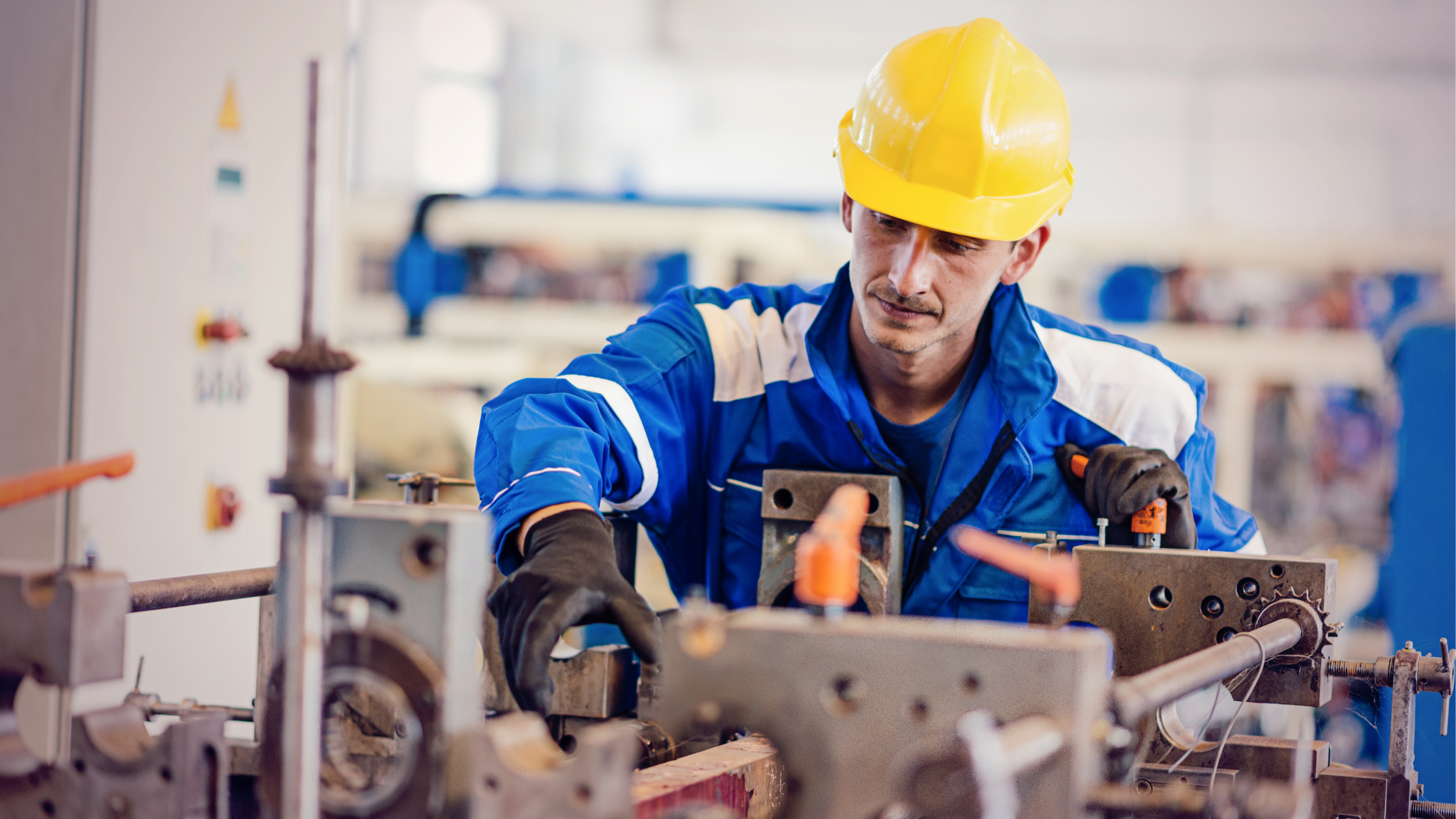 Industrial worker wearing a hard hat and protective gloves operates machinery inside a manufacturing facility.