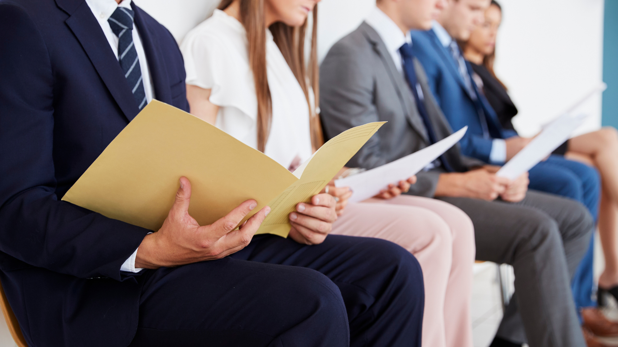 Professionally dressed job candidates seated in a row reviewing resumes and documents while waiting for an interview.