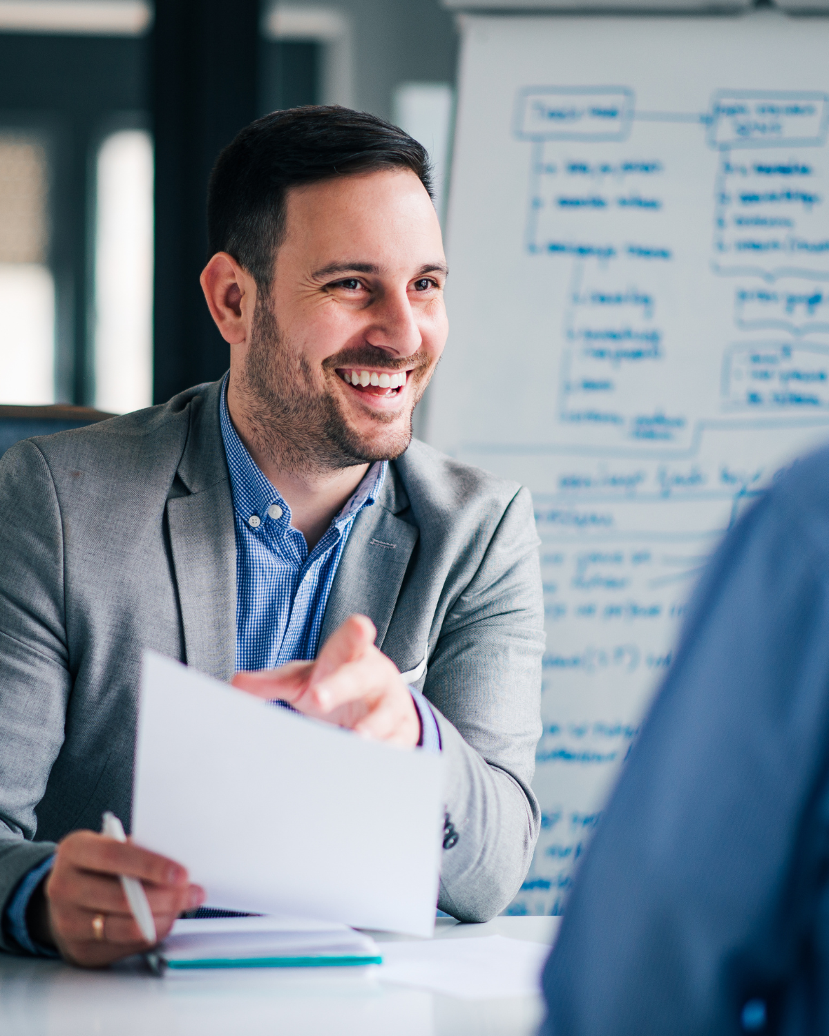 Construction worker wearing a high-visibility safety vest and glasses holds a hard hat while standing at a job site, smiling confidently.