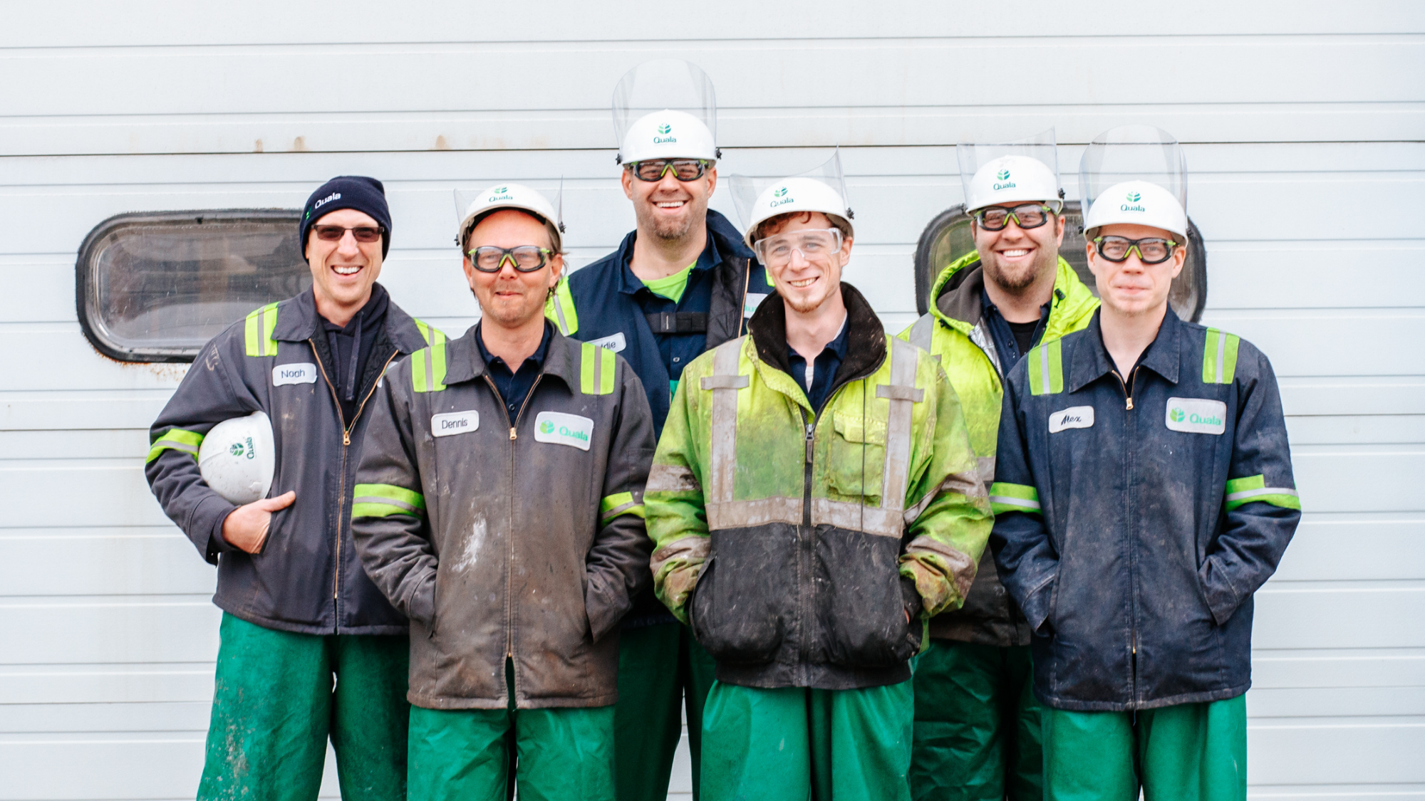 A group of six industrial laborers smiling at the camera wearing PPE.