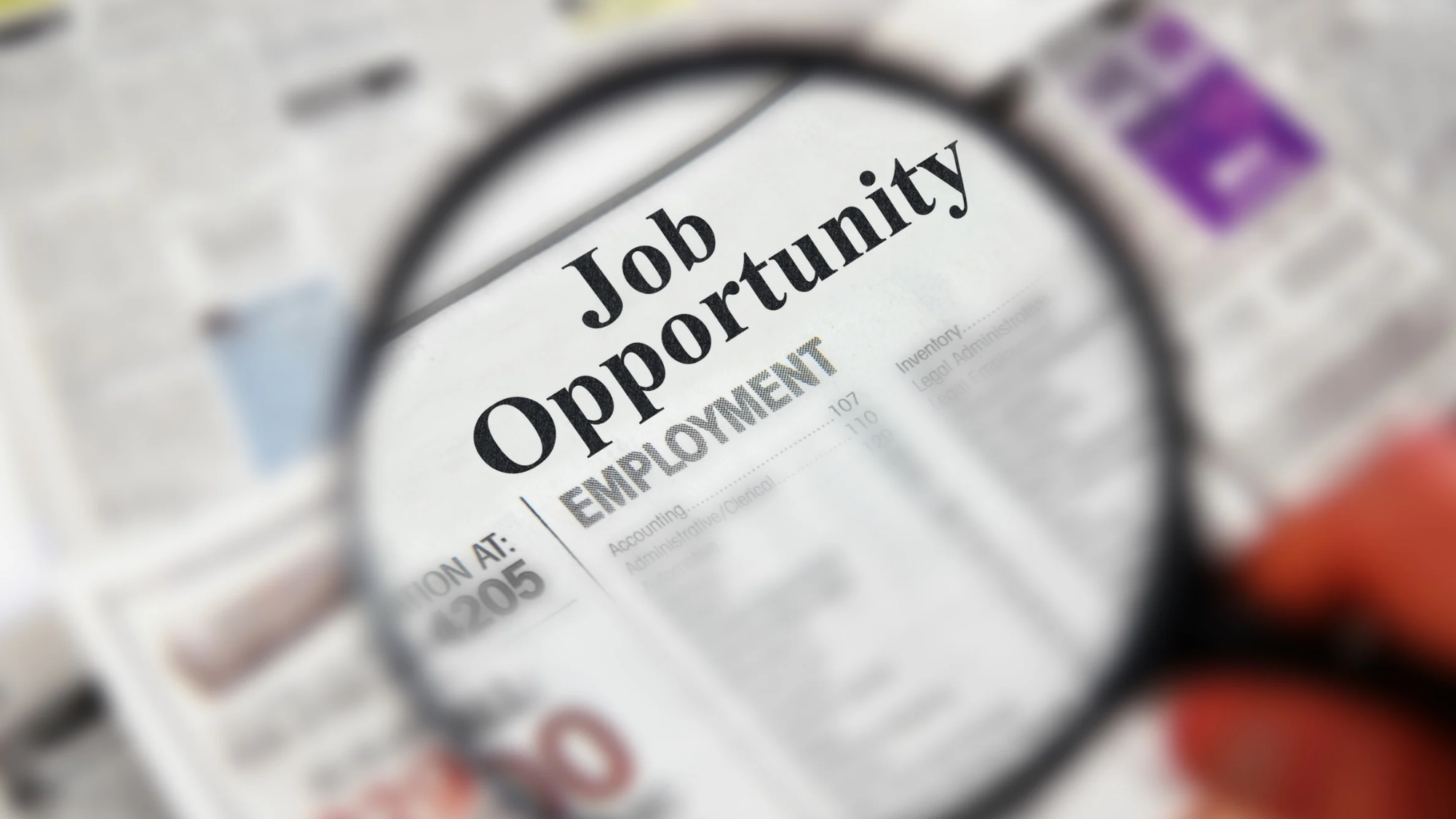Magnifying glass highlighting the words “Job Opportunity” and “Employment” in a newspaper’s classified job listings.
