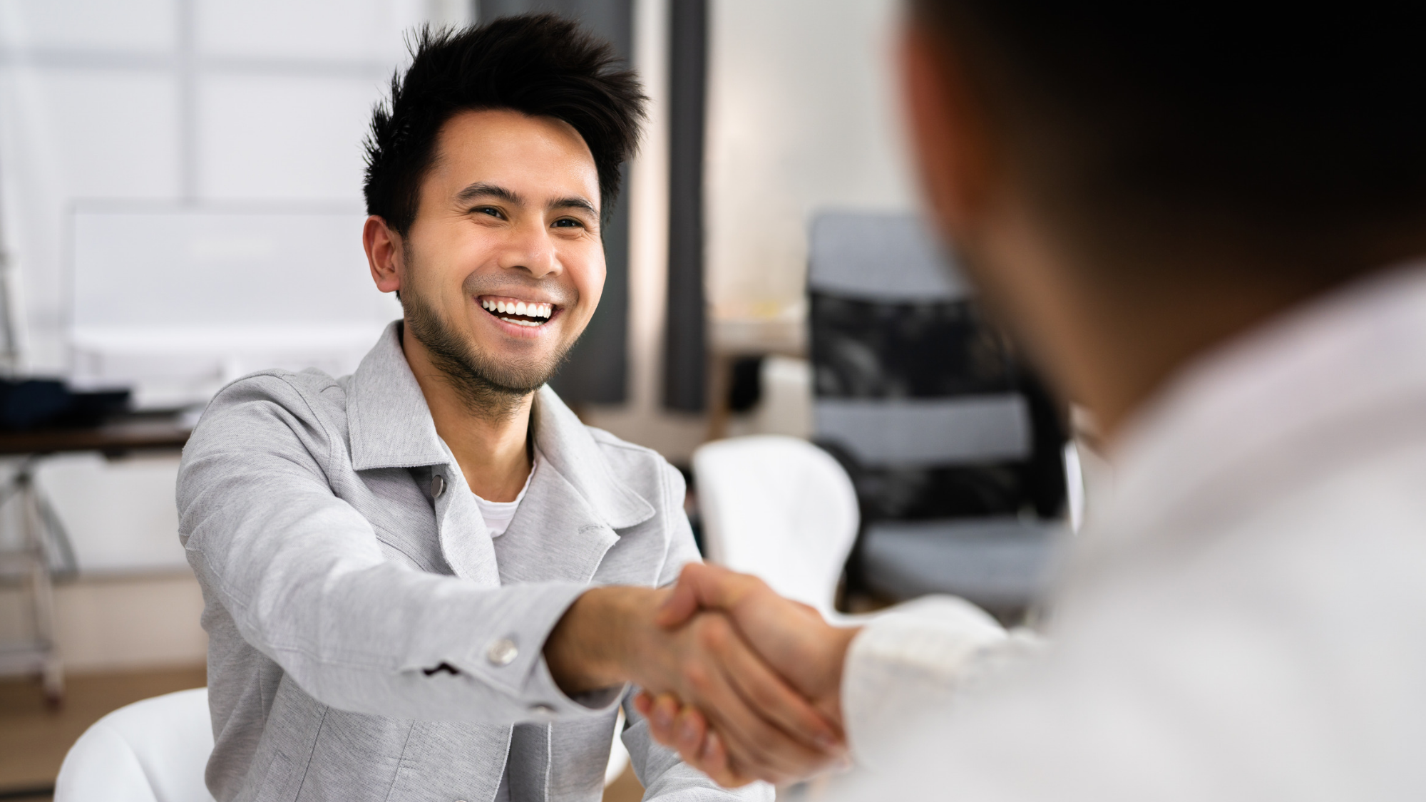 Smiling job candidate shakes hands with another person during a professional meeting or job interview in a modern office.